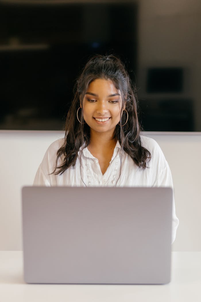A teenager studying indoors with a laptop, showing focus and diligence.